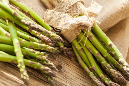 Fresh healthy green asparagus as a close-up on a wooden table in sunlight