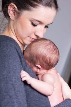 Happy young mother holds her newborn child in front of her chest and smiles