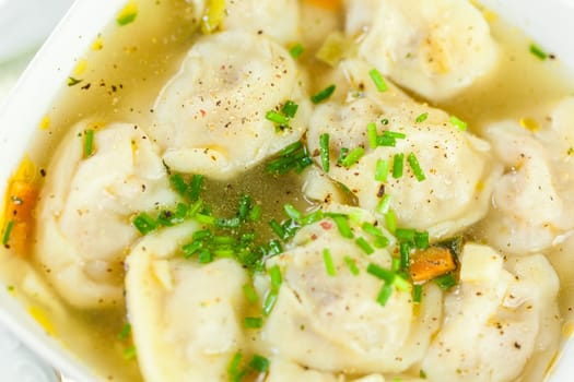 Bowl with Russian Pelmeni Italian tortellini with broth and parsley close-up on a wooden table