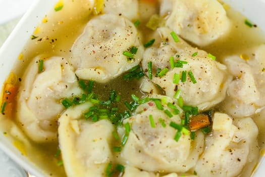 Bowl with Russian Pelmeni Italian tortellini with broth and parsley close-up on a wooden table