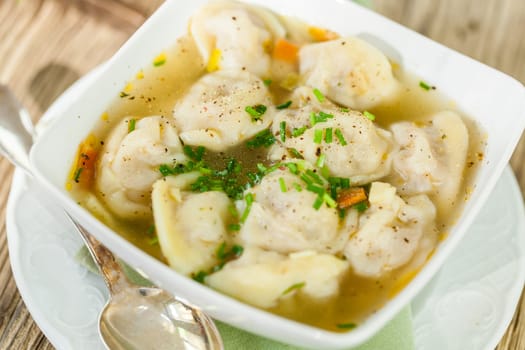Bowl with Russian Pelmeni Italian tortellini with broth and parsley close-up on a wooden table