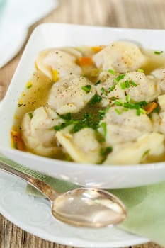 Bowl with Russian Pelmeni Italian tortellini with broth and parsley close-up on a wooden table