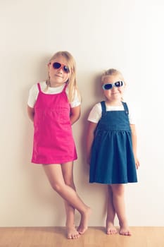 Two little girls posing in front of a walll. Studio shot.