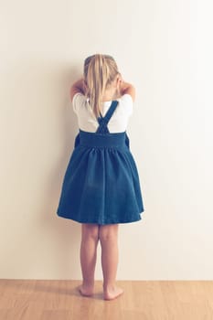 portrait of sad little girl standing near wall. studio shot