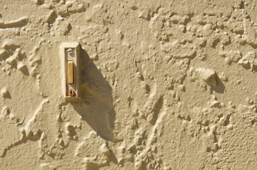 close up of old electronic doorbell, painted on outdoor wall with morning shadow.