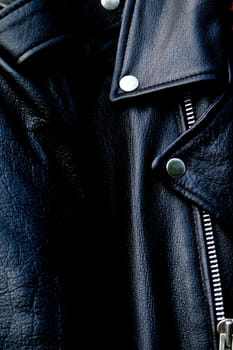 High contrast close up of black leather biker jacket showing zipper, shoulder and snap collar and lapel in sunshine.