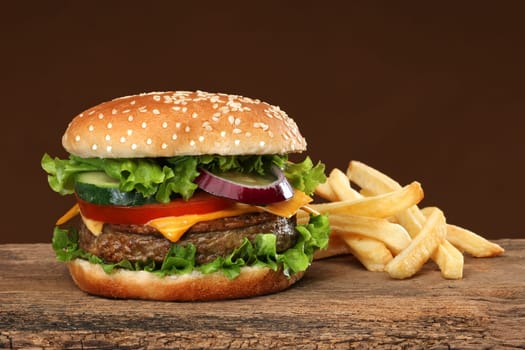Tasty hamburger and french frites on wood background.