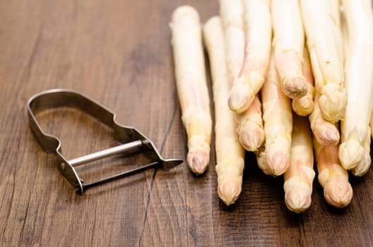 White asparagus and peeler on brown wood