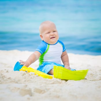 Cute baby on the tropical beach playing toys
