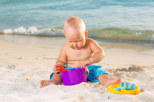 Cute baby on the tropical beach playing toys