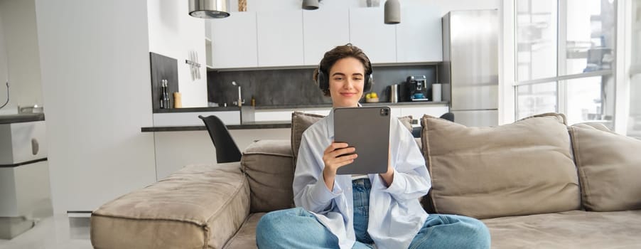 Portrait of happy woman watching video on tablet in headphones, working from home using her digital device, listening to music while reading e-book.