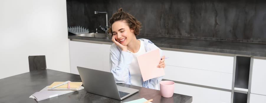 Portrait of young professional woman, works from home, looks at laptop, studies online, connects to a webinar, work remote meeting via computer, video chats with tutor from courses website.
