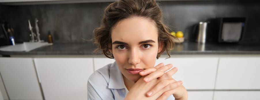 Close up portrait of young woman, 25 years old, sitting in her kitchen alone, express candid happiness, smiles, leans head on hands.