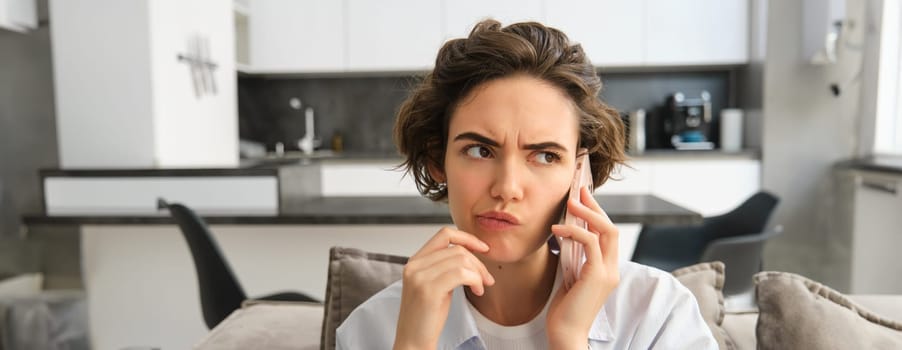 Close up portrait of woman talking on mobile phone with troubled face, listening to complicated conversation, thinking while calling someone.