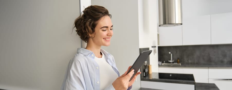 Portrait of woman smiling, looking at her digital tablet, reading message, watching videos online, working from home. Copy space