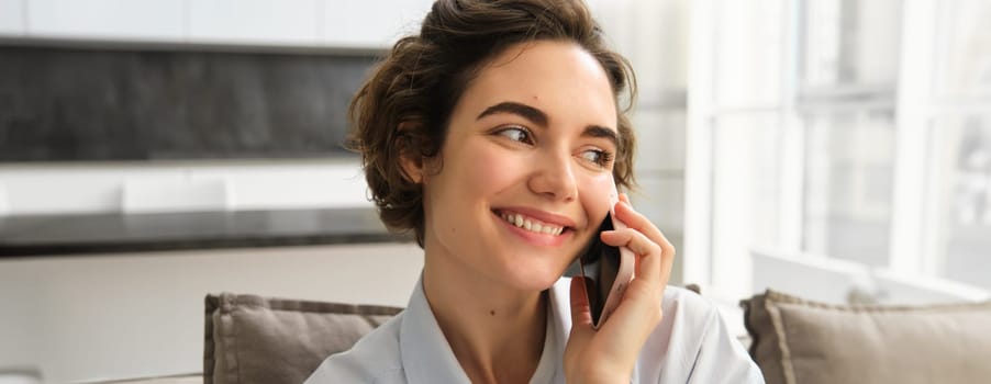 Close up portrait of smiling beautiful woman, talking on mobile phone, chats on smartphone, calls someone, sits at home.