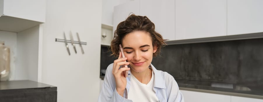 Portrait of beautiful girl talks on mobile phone, has conversation, answer a call in kitchen.