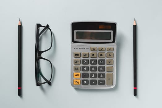 Top view of calculator, glasses, pen and green plant on blue office desk