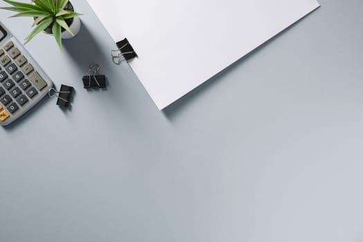 Top view of blank notebook, pen, calculator and green plant on grey office desk