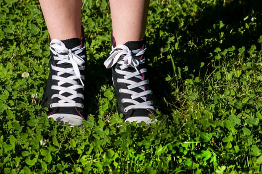 Girl legs with sneakers on fresh green grass background