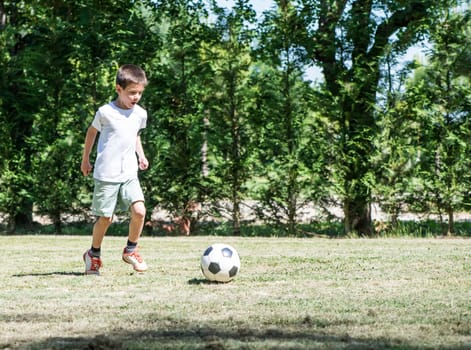 Child playing football in a stadium. Trees on the background
