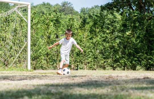 Child playing football in a stadium. Trees on the background