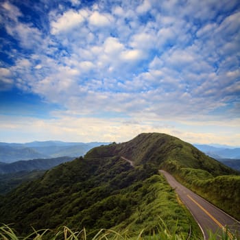 asphalt road through the green field and clouds on blue sky in summer day