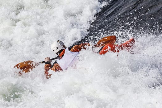 an active male kayaker rolling and surfing in rough water