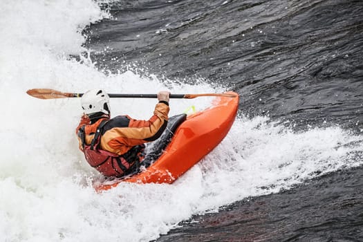 an active male kayaker rolling and surfing in rough water