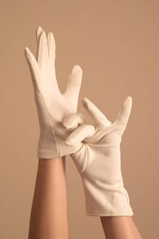 A woman's hands and forearms are shown as she models a vintage pair of formal white knit gloves. She is using one gloved hand to pull on the other glove.