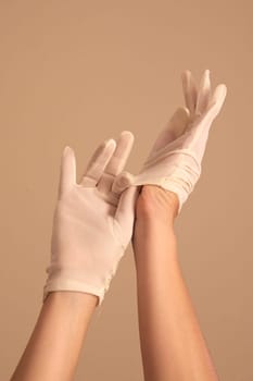 A woman's hands and forearms are shown as she models a vintage pair of formal white gloves. She is using one gloved hand to pull the glove onto the other hand.