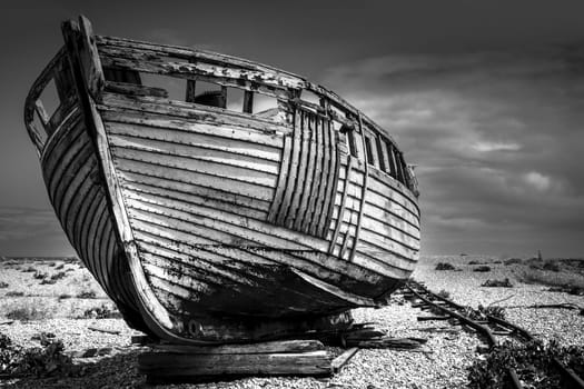 An old abandoned fishing boat stranded on a beech in black and white.