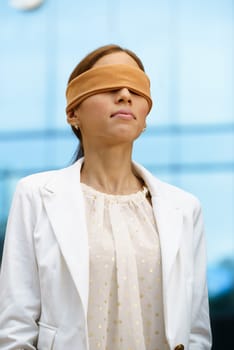 Concept of future and forecasting. Portrait of latina blindfolded businesswoman near office building