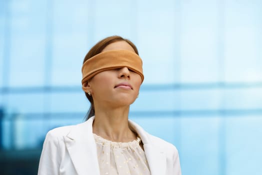 Concept of future and forecasting. Portrait of latina blindfolded businesswoman near office building