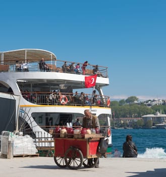 Old man selling drinks and foods on the karakoy pier in Istanbul in front of a leaving ferry boat.Eating on the street is part of local life here