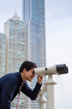 Portrait of young chinese business man standing in Panama City and looking through binoculars. Concept of forecasting, career, success