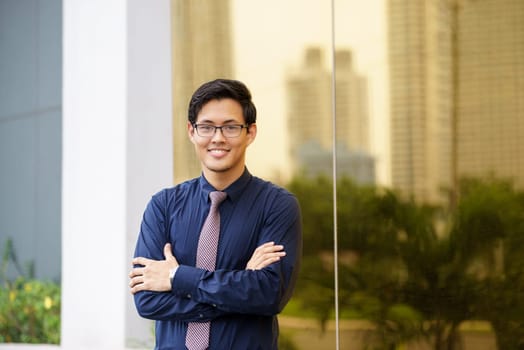 Portrait of chinese businessman standing with arms crossed near office building in Panama. Reflections of city on mirror