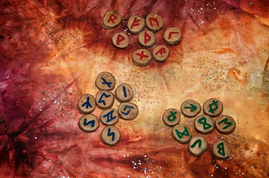 three sets of wooden fortune telling runes, an ancient alphabet known as the futhark are on a colorful hand dyed fabric with small sparkling beads..Note