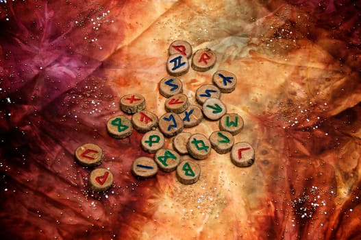 hand carved and painted wooden runes, an ancient alphabet known as the futhark, are on a colorful hand dyed fabric with small sparkling beads..Note