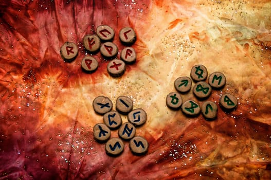 set of wooden runes, an ancient alphabet known as the futhark are divided into the three aetts, on a colorful hand dyed fabric with small sparkling beads..Note