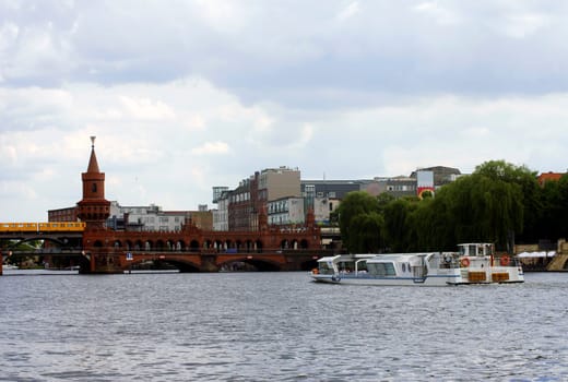 Berlin,Germany – June 16,2014: A yellow tram crosses the Warsaw Bridge over the Spree river on which a passenger ship sails on June 16,2014 in Berlin.
