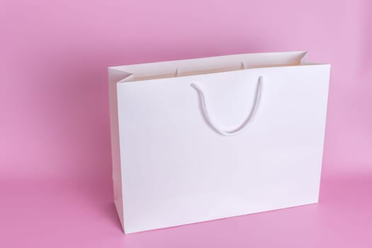 A large white paper bag with white rope handles stands on a pink background in close-up. Copy space. Mock up. Top view