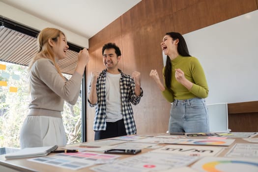 A joyful team of three celebrates their success in a bright office, highlighting teamwork and collaboration.