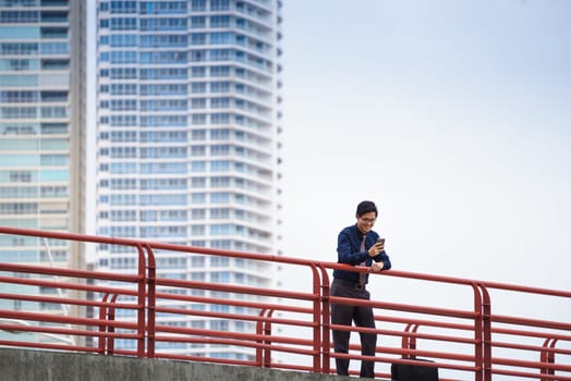 Portrait of chinese businessman on bridge in Panama city with skyline in background, reading emails on smartphone