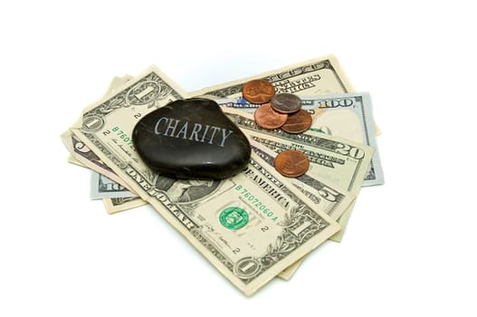 A stone with the word Charity engraved on it, rests on a fanned stack of dollar bills and change. Over white.