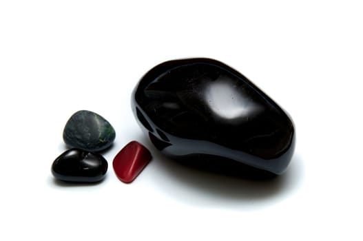 A collection of four smooth dark rocks used for massage over white. One large rock and three small.