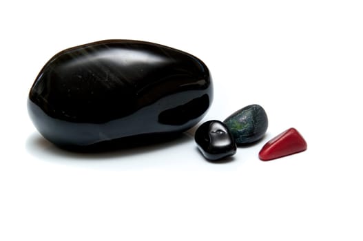 A collection of four smooth dark rocks used for massage over white. One large rock and three small.