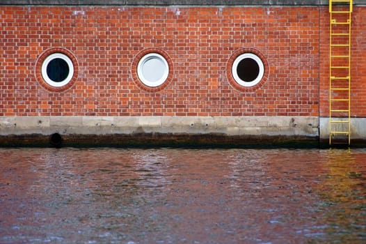 The photograph of a river boundary of bricks,with a ladder and round windows.