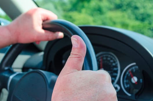 Hand on the steering wheel,the other hand shows the thumbs up.