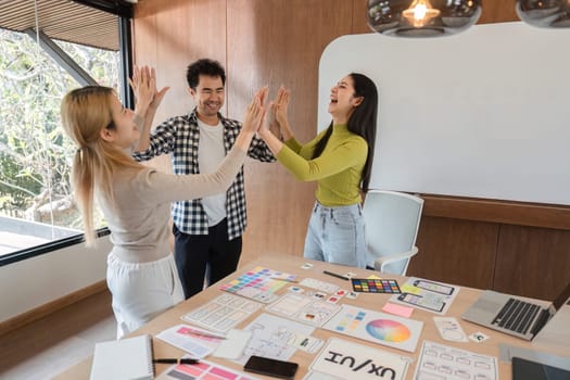 Three enthusiastic colleagues high-five in a vibrant office, illustrating teamwork and creative collaboration.